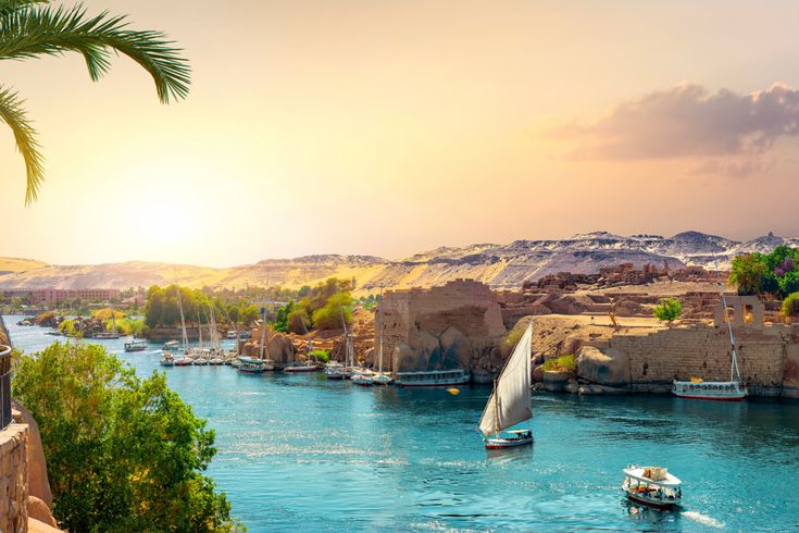 Segelboote und kleine Schiffe auf dem Nil in Ägypten bei Sonnenuntergang, mit Ruinen und Sanddünen im Hintergrund
