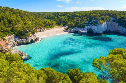 Idyllische Bucht Cala Mitjaneta auf Menorca mit weißem Sandstrand, türkisfarbenem Wasser und von Klippen umgeben
