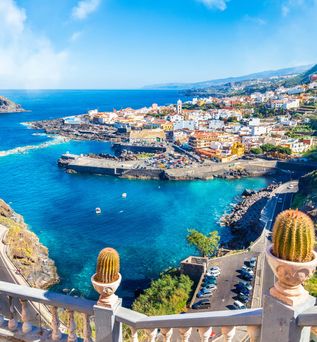 Blick von einer Terrasse auf eine Bucht am blauen Meer mit einem Felsen im Hintergrund im Wasser