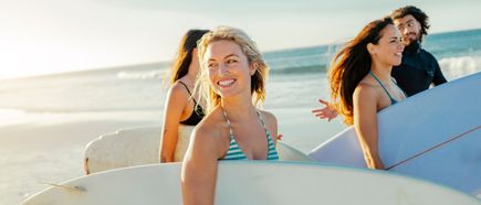 Mehrere Personen tragen Surfboards und gehen gemeinsam am Strand entlang, mit Meer und Wellen im Hintergrund