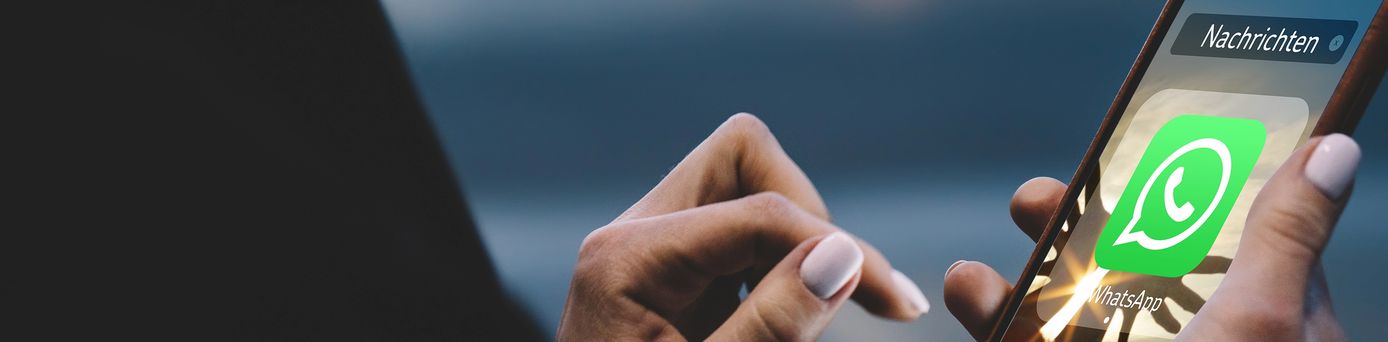 Nahaufnahme einer Hand, die ein Smartphone mit geöffneter WhatsApp‑App und Nachrichten‑Ansicht hält