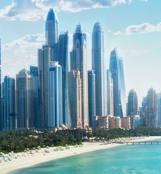 Blick auf eine Küstenstadt mit hohen, modernen Wolkenkratzern und einem Strand mit Palmen am Meer.