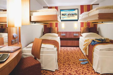 Innenkabine der AIDAstella mit zwei unteren Betten, zwei oberen Klappbetten, modernem Holzmobiliar, einem Schreibtischbereich und farblich abgestimmter Bettwäsche sowie Dekoration