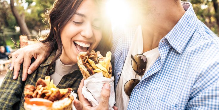 Junges Paar isst Kebab im Fladenbrot im Freien, lacht und hält die gefüllten Wraps in der Hand