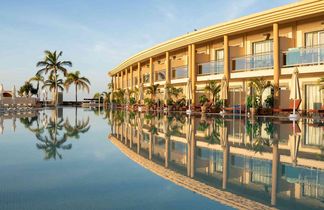 Großer Außenpool mit klarem Wasser, umgeben von Liegestühlen und Sonnenschirmen, blauer Himmel mit wenigen Wolken.