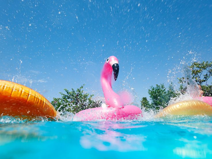 Pinker Flamingo-Schwimmreifen im Pool mit Wasserspritzern und blauem Himmel