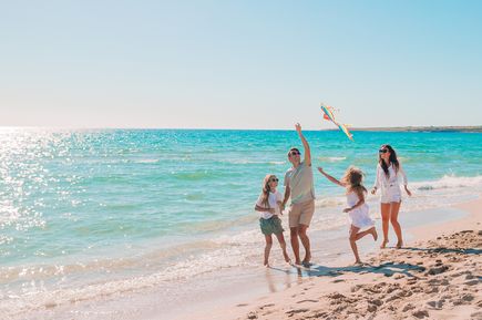 Familie mit zwei Kindern spielt am Strand. Vater lässt einen Drachen steigen.
