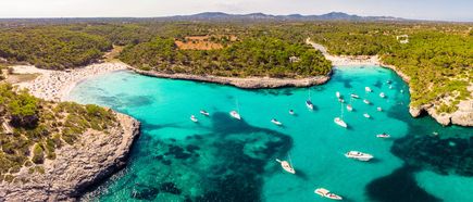 Luftaufnahme der Bucht Cala Mondragó auf Mallorca mit türkisblauem Wasser, Booten im Meer und von grünen Pinienwäldern umgebenen Stränden