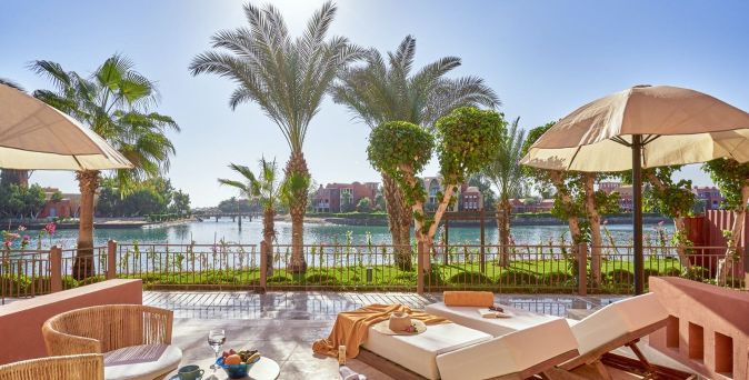 Terrasse mit Liegestühlen und Sonnenschirmen, Blick auf Palmen und Wasserkanal im Three Corners Ocean View Hotel