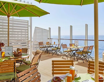 Außenterrasse eines AIDA-Schiffs mit Holztischen und Stühlen, Sonnenschirmen und Blick auf das Meer