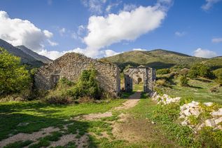 Ruinen aus Naturstein in einer grünen Hügellandschaft unter blauem Himmel mit Wolken