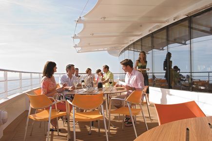 Gäste sitzen auf der Außenterrasse des Bella Vista Restaurants der AIDAbella, an gedeckten Tischen unter einem schattenspendenden Dach mit Blick auf das Meer