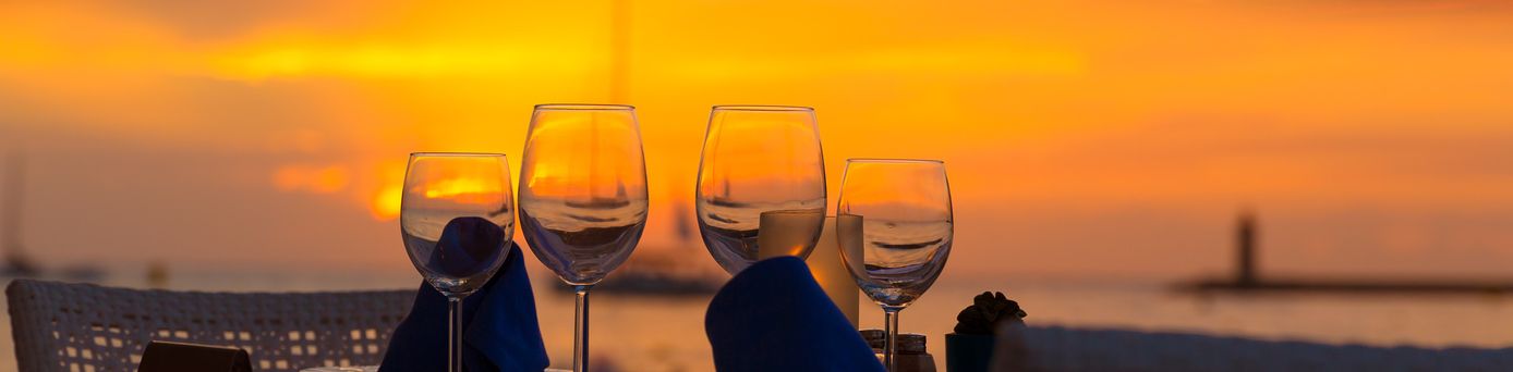 Weingläser auf einem Tisch vor einem orangefarbenen Sonnenuntergang am Wasser