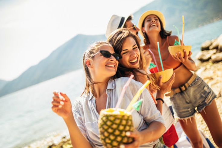 Gruppe junger Leute am Strand mit exotischen Cocktails, lachend und tanzend in der Sonne