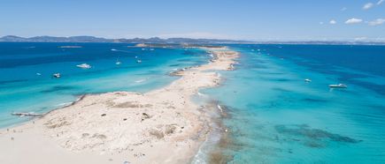Am Strand Ses Illetes auf Formentera zieht sich eine schmale Sandzunge zwischen türkisblauem Meer entlang, während Boote vor der Küste ankern