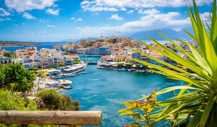 Blick auf den Hafen von Agios Nikolaos auf Kreta mit bunten Häusern, blauem Meer und lebendiger Uferpromenade unter sonnigem Himmel