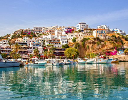 Blick auf eine Küstenstadt mit weißen Gebäuden und bunten Blumen, umgeben von Wasser und Booten im Vordergrund.