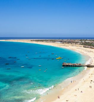 Strand Sotavento auf Fuerteventura mit hellem Sand, klarem türkisfarbenem Wasser, vielen kleinen Booten und einem Steg mit Menschen.