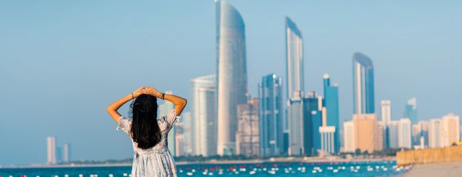 Frau steht am Strand und blickt auf die Skyline von Abu Dhabi