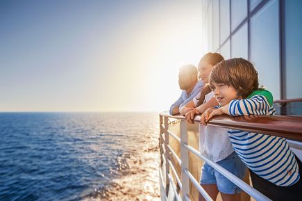 Familie lehnt an der Reling der AIDAblu und blickt auf das Meer bei tief stehender Sonne, mit glitzernder Wasseroberfläche im Hintergrund