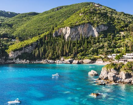 Bucht von Paleokastritsa in Griechenland mit klarem blauem Wasser, umgeben von grünen Hügeln und Felsen, zwei kleinen Booten auf dem Wasser