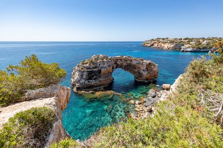Es Pontas, ein natürlicher Felsbogen an der Küste von Mallorca, umgeben von klarem, türkisfarbenem Wasser und grüner Vegetation
