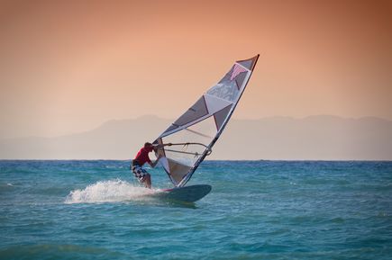 Sportler beim Kitesurfen auf dem Meer bei untergehender Sonne und Wellen