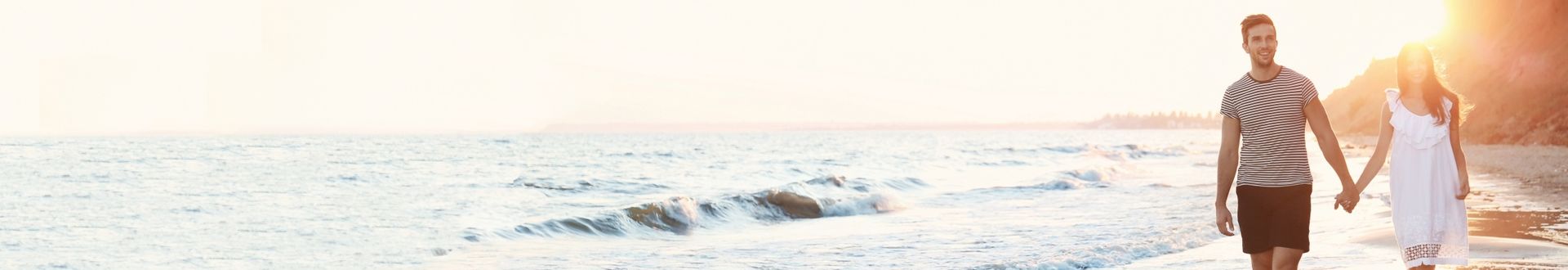 Paar geht Hand in Hand am Strand entlang, während sanfte Wellen ans Ufer rollen und die tiefstehende Sonne warmes Licht über die Szene wirft