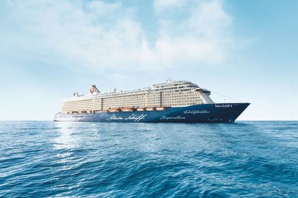 Das Kreuzfahrtschiff Mein Schiff 4 gleitet über das ruhige blaue Meer unter einem hellen Himmel, gut sichtbar mit seinem dunkelblauen Rumpf und modernen Außendecks
