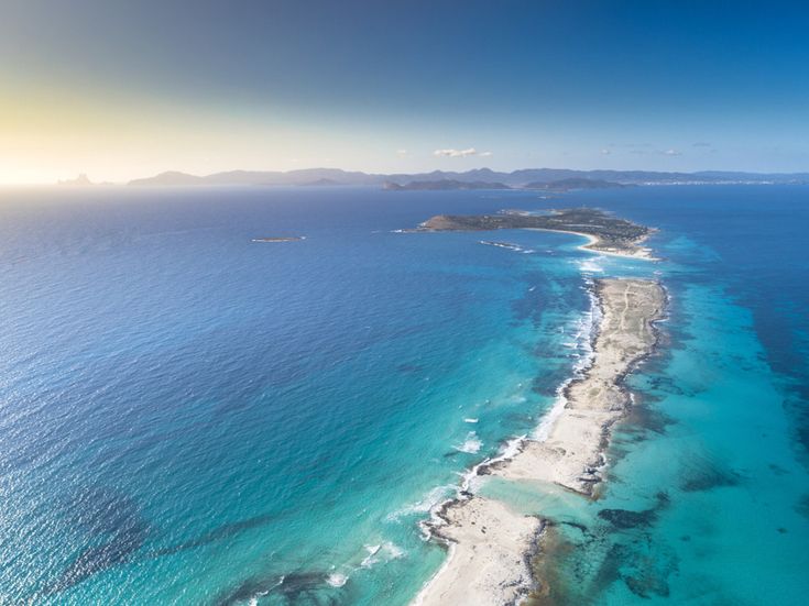 Luftaufnahme der schmalen Sandbank Ses Illetes auf Formentera, umgeben von türkisblauem Meer und mit Blick auf die Nachbarinseln