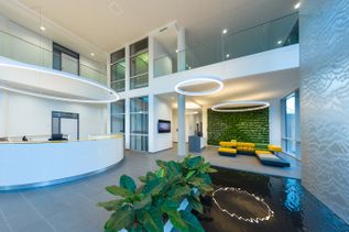 Großzügiger Empfangsbereich im Gebäude 3 von schauinsland-reisen mit Empfangstresen, Pflanzen, Sitzbereich, Wasserbecken und ringförmigen Deckenleuchten auf mehreren Ebenen