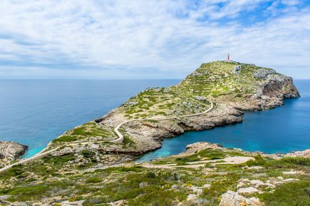 Küstenansicht von Cabrera, Mallorca, mit einem Leuchtturm auf einem Hügel, umgeben von klarem Wasser und bewachsenen Felsen