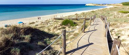 Holzsteg durch die Dünen zum Strand von Son Bou auf Menorca mit weißem Sand und türkisblauem Wasser