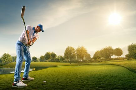 Person führt einen Golfschlag auf einem gepflegten Golfplatz mit Fairway, Grünfläche und tief stehender Sonne im Hintergrund aus