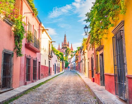 Bunte koloniale Häuserfassaden in Mexiko in einer engen Kopfsteinpflasterstraße mit einer großen Kirche im Hintergrund.