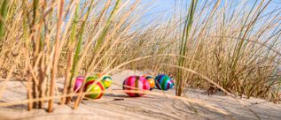 Bunte Ostereier liegen im Sand zwischen Strandgras