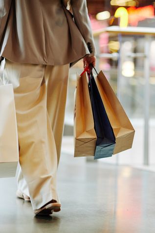 Person in heller Kleidung trägt mehrere Einkaufstüten in einem modernen Einkaufszentrum