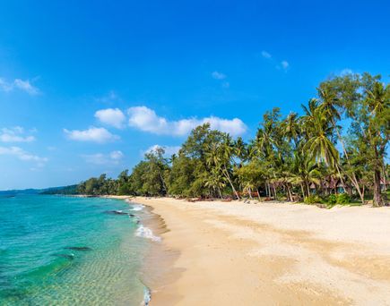 Panoramaaufnahme eines Strandes in Mauritius mit feinem Sand, klarem Wasser und Palmen. Im Hintergrund sind Bäume und Hütten sichtbar.
