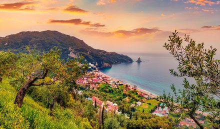 Agios Gordios auf Korfu in Griechenland mit Blick auf ein Küstendorf, einen Sandstrand, grüne Hügel und das Meer bei Sonnenuntergang.