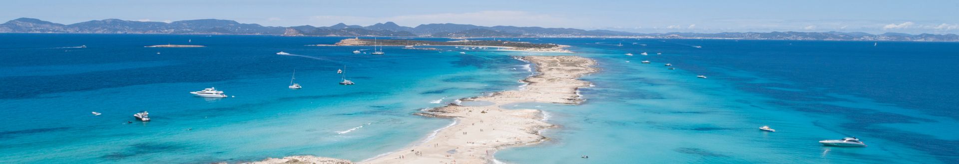 Luftaufnahme des Playa de Illetas auf Formentera mit schmaler Sandbank, türkisblauem Wasser und Booten vor der Küste