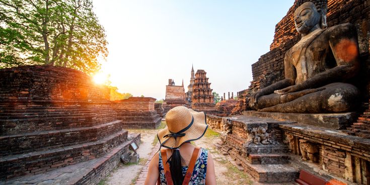 Person vor historischen Tempelruinen und einer großen Buddha-Statue im Sukhothai Historical Park beim Wat Si Chum Tempel in Thailand