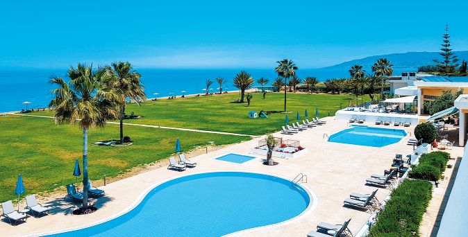 Poollandschaft des Natura Beach Hotel & Villas mit Palmen, großer Gartenanlage und direkter Lage am naturbelassenen Strand auf Zypern.