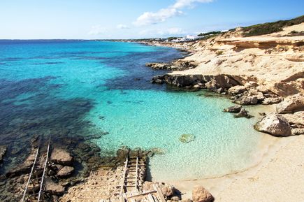 Türkisfarbenes Meer bei Es Caló auf Formentera mit felsiger Küste, hellem Sandstrand und alten Holzstegen am Ufer