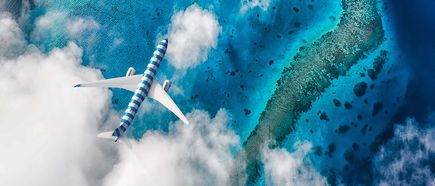 Condor Airbus A330neo im blau‑weiß gestreiften Design über den türkisfarbenen Gewässern der Malediven, teilweise von Wolken umgeben