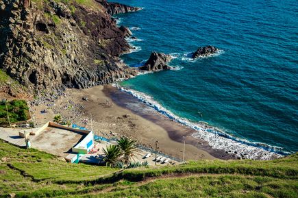 Blick auf den Prainha Beach auf Madeira mit dunklem Sandstrand, türkisfarbenem Meer, steilen Felsklippen und einer geschützten Badebucht