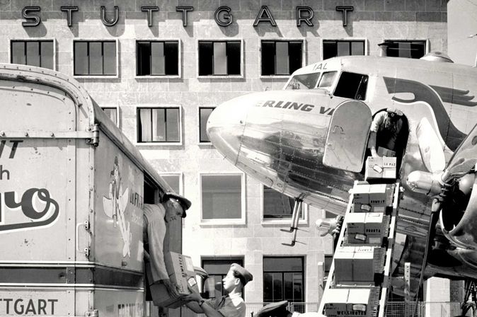 Historische Frachtverladung am Flughafen Stuttgart im Jahr 1949 mit Propellerflugzeug, Frachtfahrzeug und Bodenpersonal vor dem damaligen Flughafengebäude