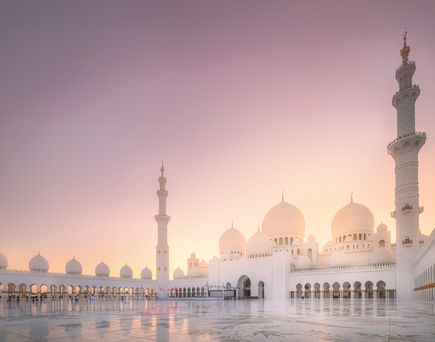 Weitläufiger Innenhof der Scheich-Zayid-Moschee in Abu Dhabi bei Sonnenuntergang mit weißen Kuppeln und hohen Minaretten.