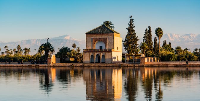 Historisches Gebäude am Ufer eines ruhigen Sees mit Palmen und Bergen im Hintergrund bei klarem Himmel