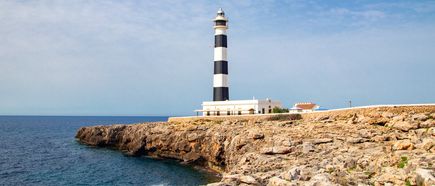 Schwarz-weiß gestreifter Leuchtturm am Cap d’Artrutx auf Menorca auf einer felsigen Landzunge am Meer