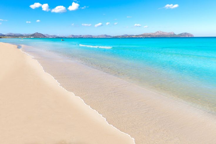 Weißer Sandstrand von Can Picafort auf Mallorca mit türkisblauem Wasser und Bergkulisse im Hintergrund